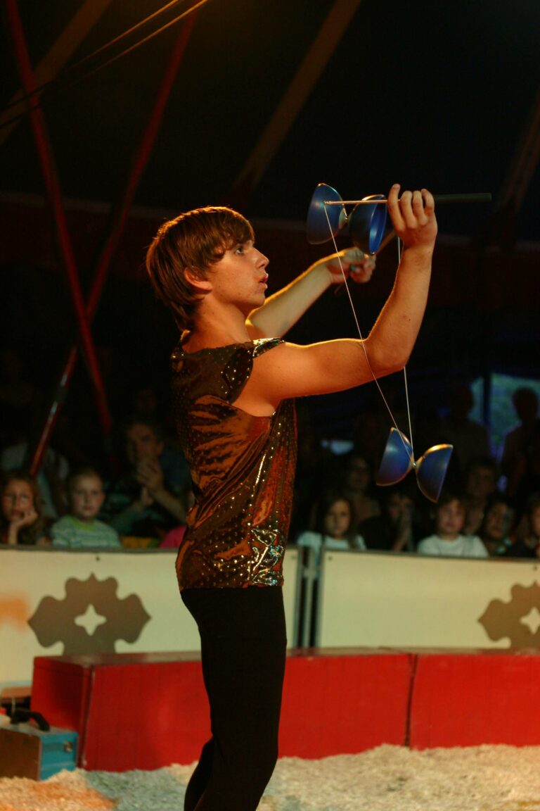 Bastian steht in der Manege und spielt zwei Diabolos um den Arm.